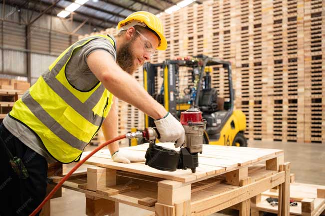 Worker using a nail gun during pallet repair